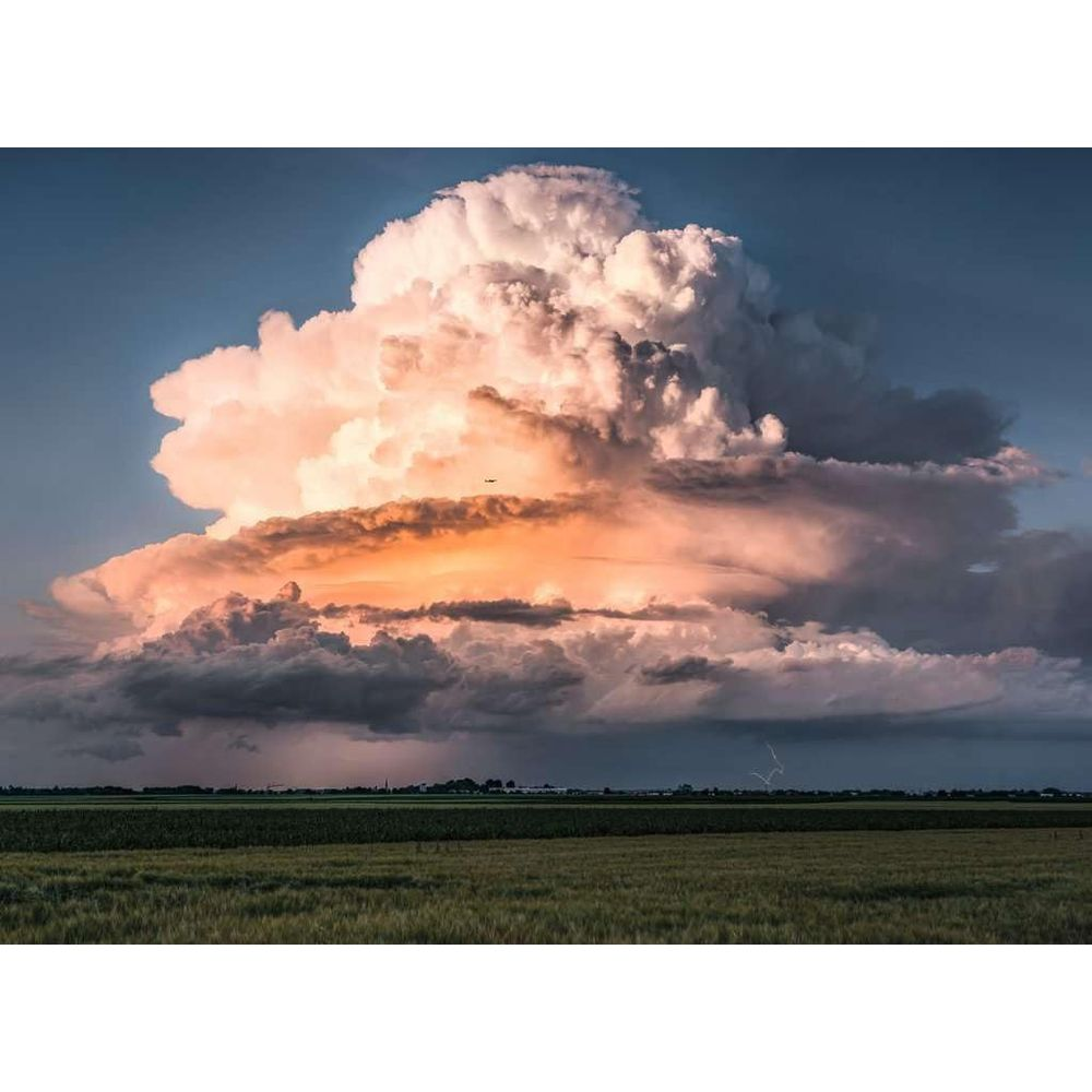 Un'enorme nuvola temporalesca rosata con fulmini su un campo.