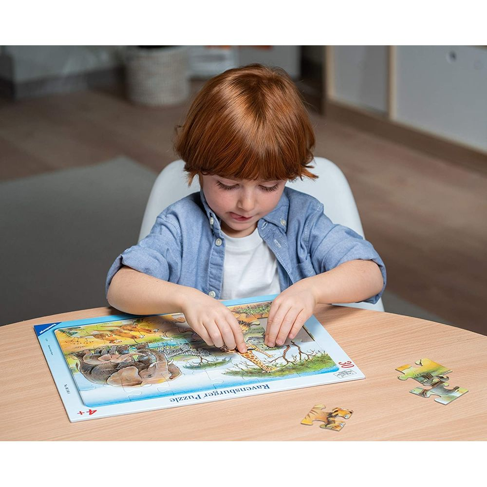 Chłopiec z rudymi włosami układa puzzle przedstawiające zwierzęta, takie jak żyrafy i zebry.