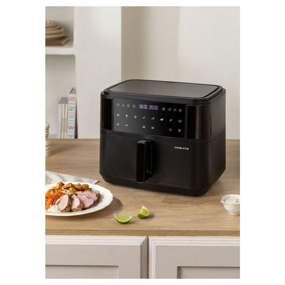Freidora de aire negra con pantalla digital, junto a un plato de carne y verduras.