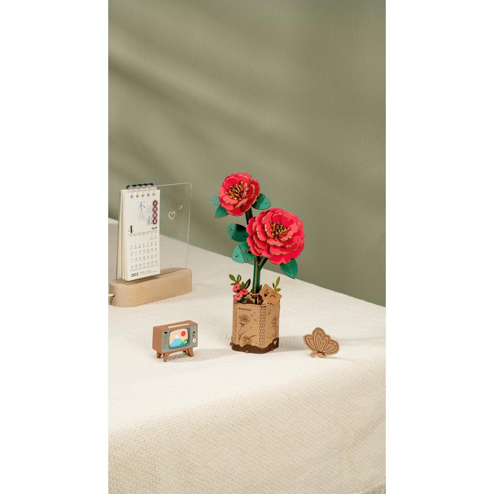 Dwa czerwone papierowe kwiaty w doniczce, obok kalendarza i mini telewizora.