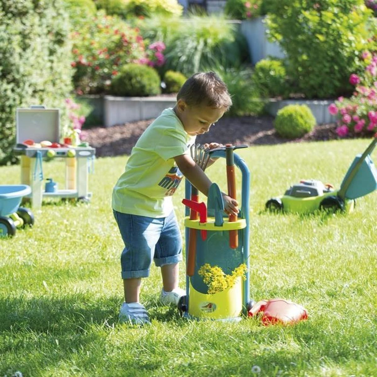 Un niño ordena herramientas de jardín junto a un cortacésped de juguete.