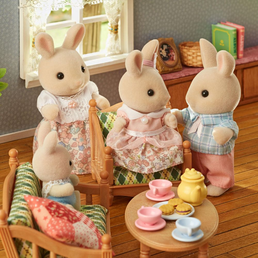 Cuatro figuras de conejos en una sala de estar de casa de muñecas tomando té.