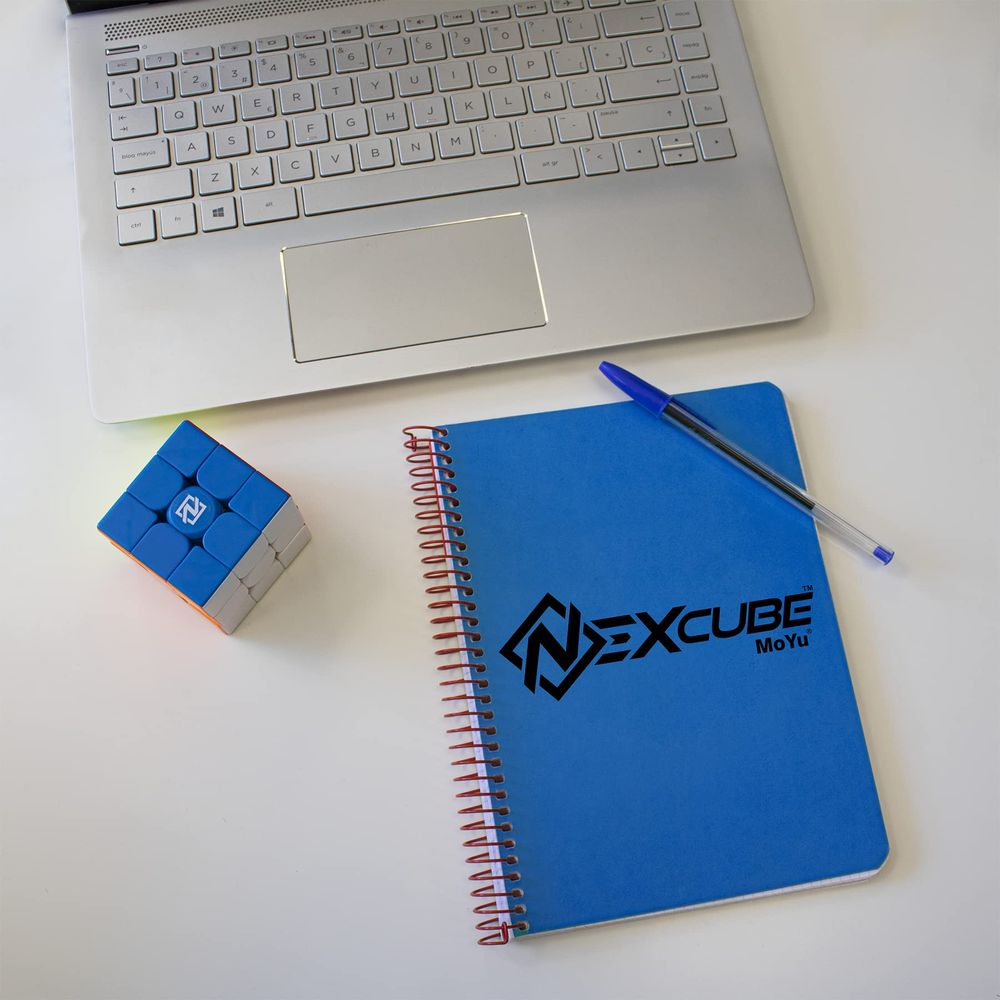 Laptop, kostka Rubika i notatnik z długopisem na białym biurku.