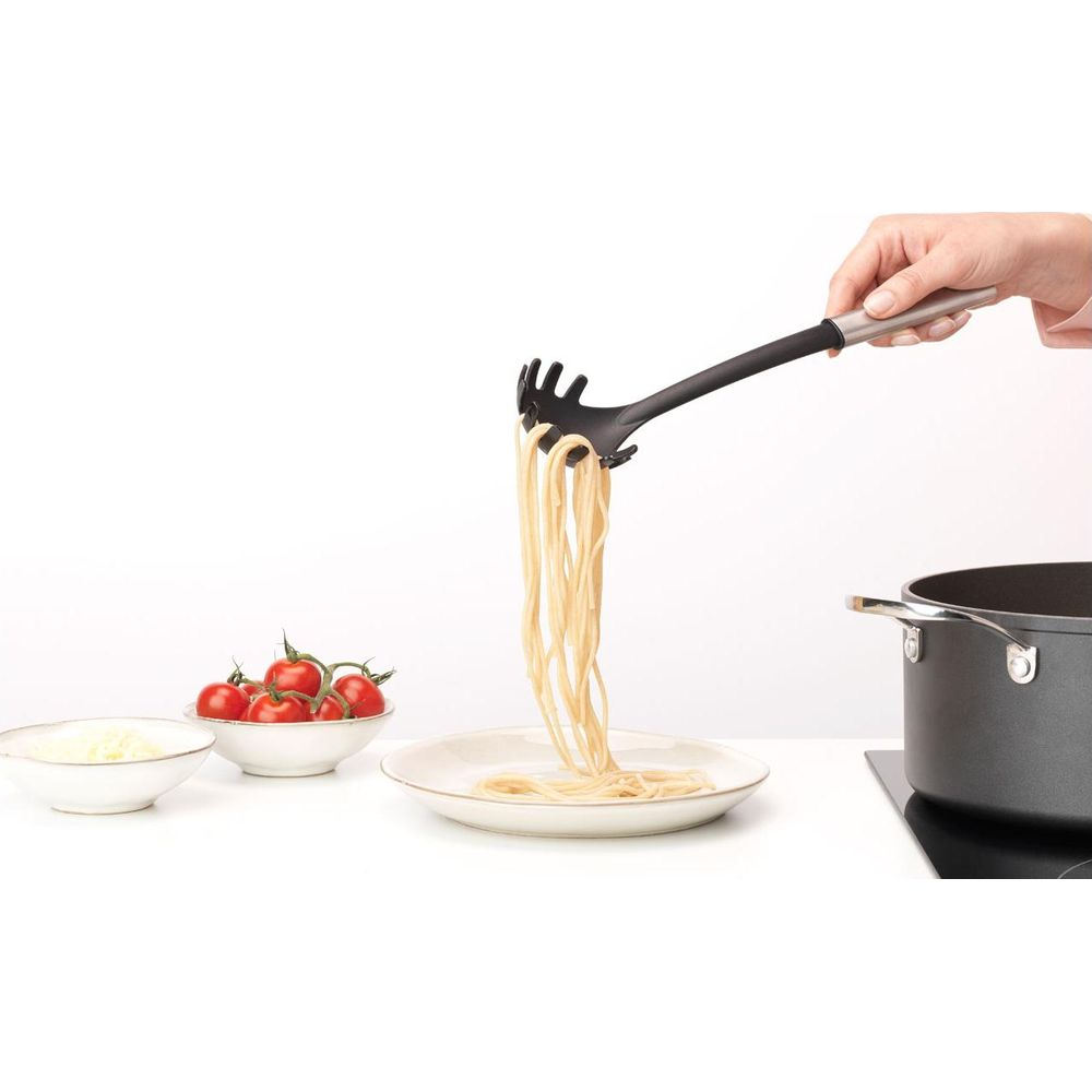 Un mestolo per spaghetti solleva la pasta in un piatto. Pomodori e formaggio nelle vicinanze.
