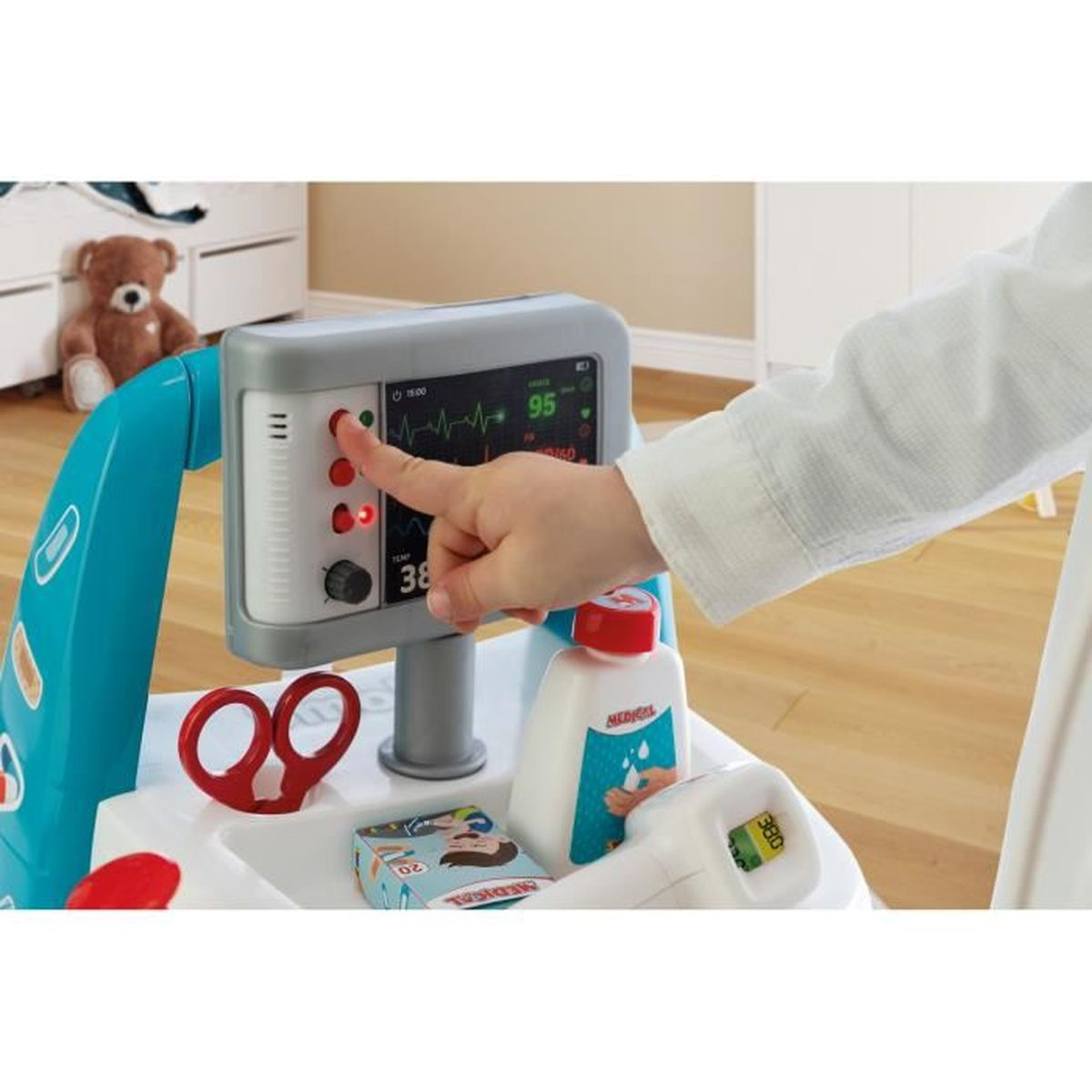 La mano de un niño presiona un monitor médico con un oso de peluche al fondo.