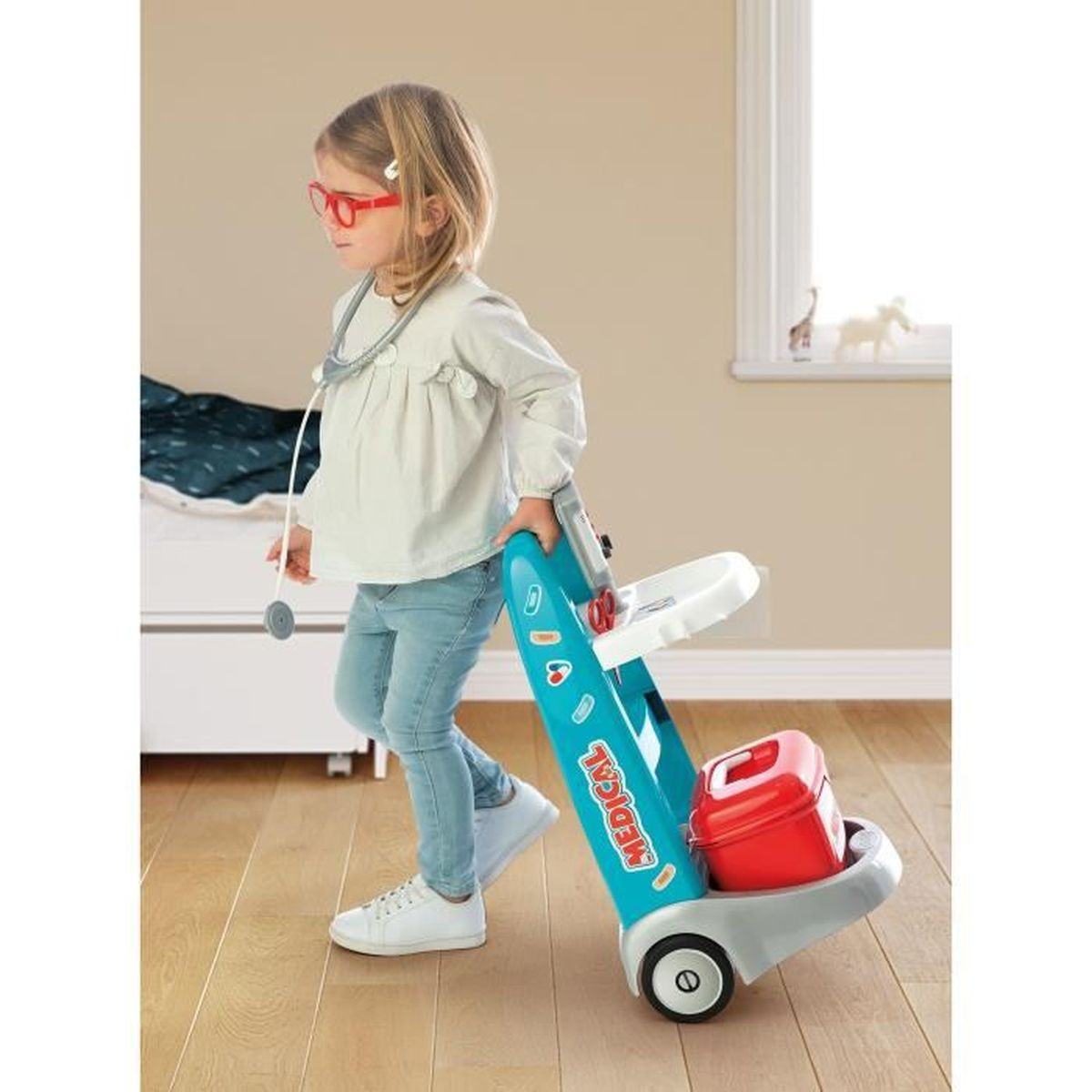 Una niña con gafas tira de un carrito médico de juguete.
