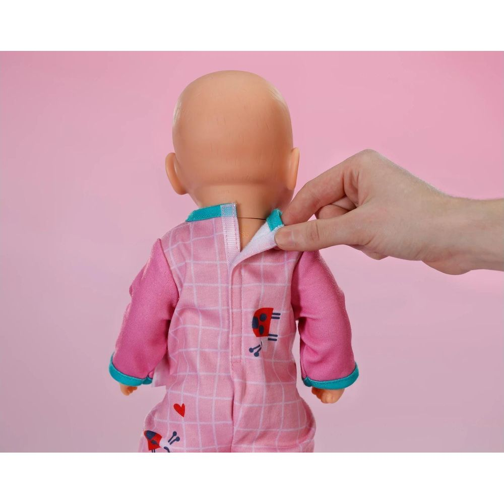 Osoba zapina różowy piżamę w kratkę na lalce.