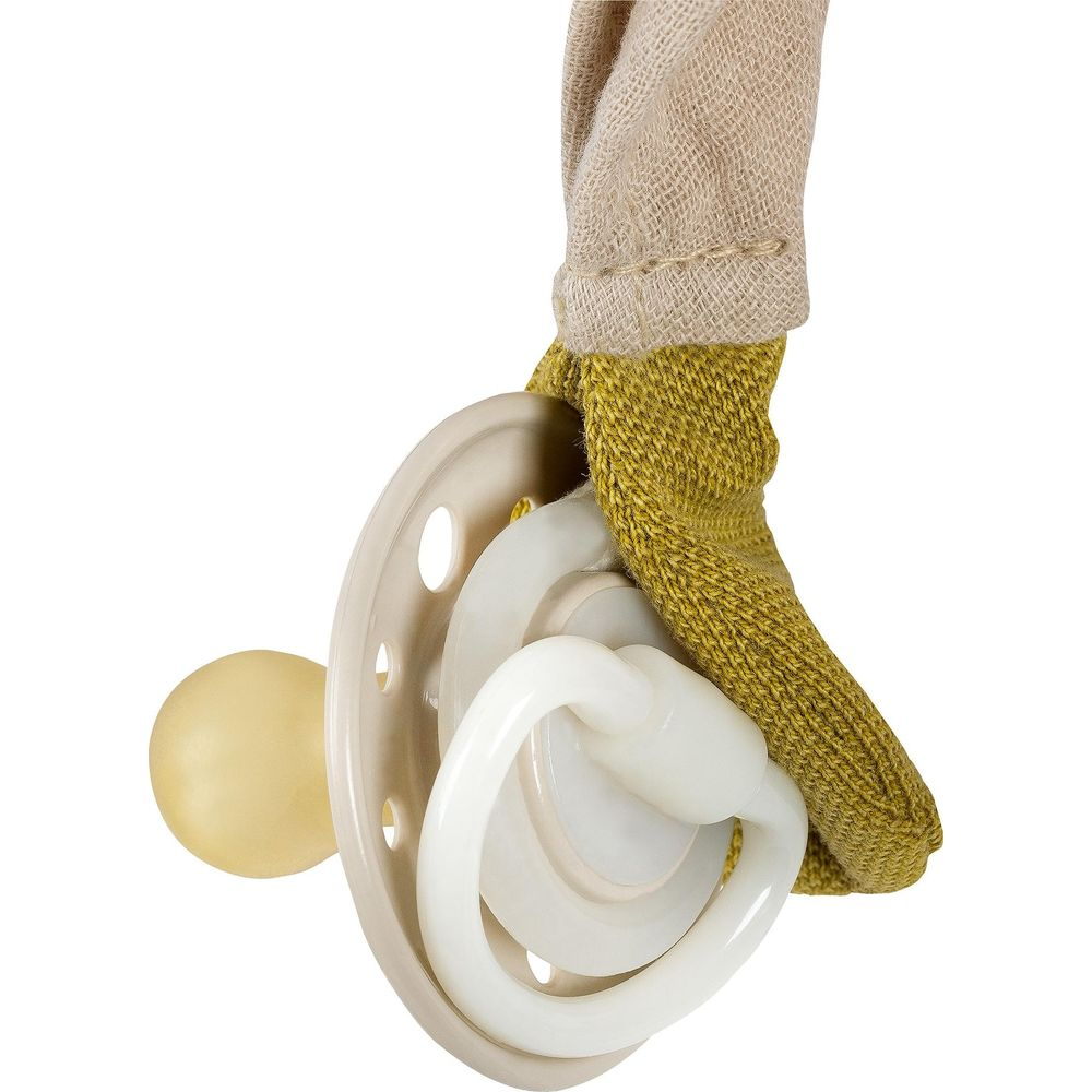 Ein beige Schnuller mit weißem Griff hängt in einem gelben Stoffbeutel.