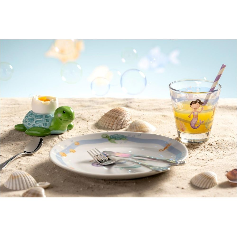 Portauovo tartaruga, piatto, bicchiere sirena e conchiglie su sabbia.