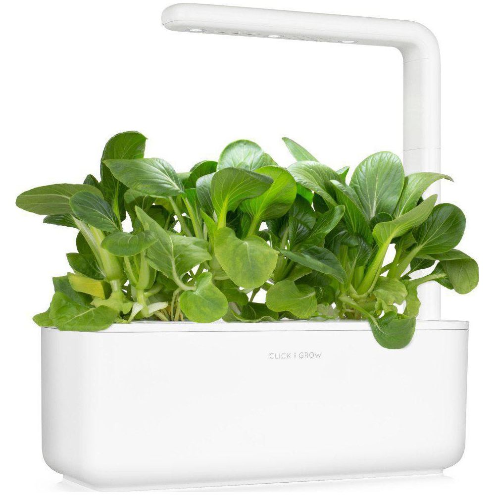 Un système de jardin intérieur blanc avec des plantes vertes sous une lampe de croissance LED.