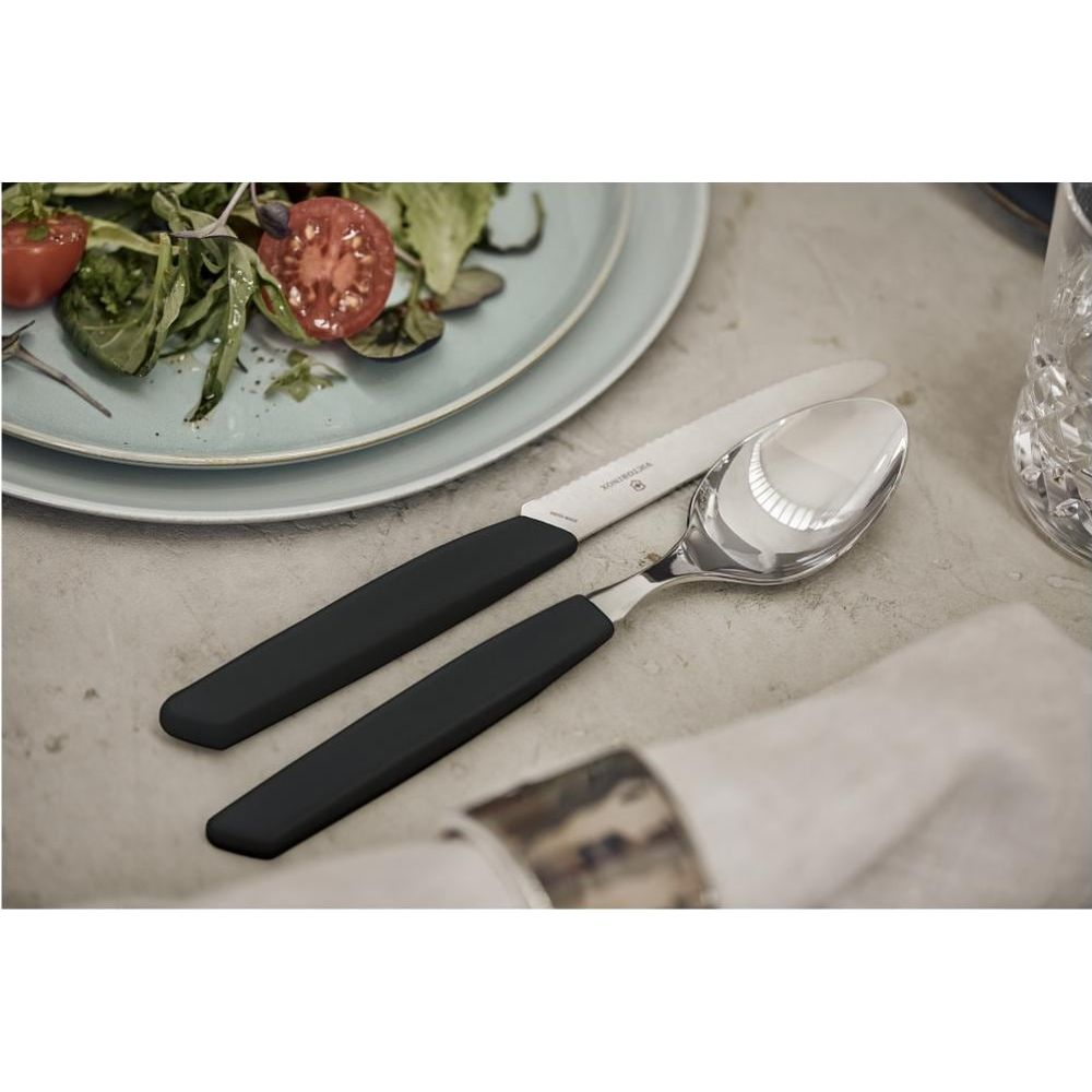 Un coltello e un cucchiaio con manici neri giacciono accanto a un'insalata su un piatto.