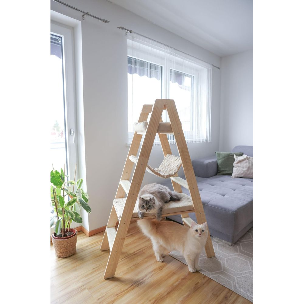 Zwei Katzen auf einem Holz-Kratzbaum vor einem Sofa und Fenster.