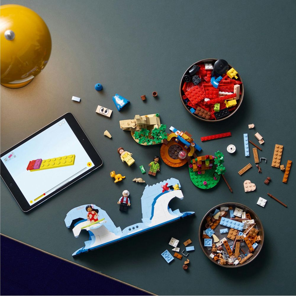 Tablet, tuğla ve figürlerle masa üzerinde Lego inşa projesi.