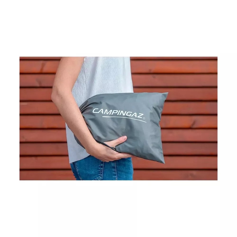 Una persona tiene una borsa grigia con il logo Campingaz contro un muro di legno.