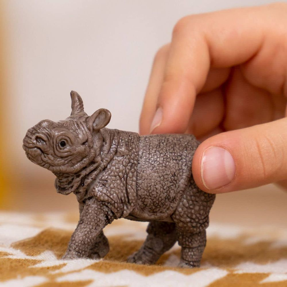 Une main tient un petit rhinocéros jouet gris à la texture de peau détaillée.