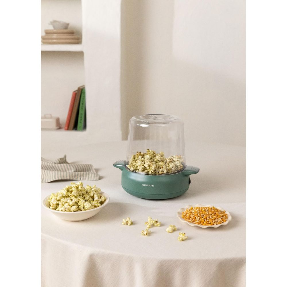 Una máquina de palomitas verde con palomitas y granos de maíz sobre una mesa.