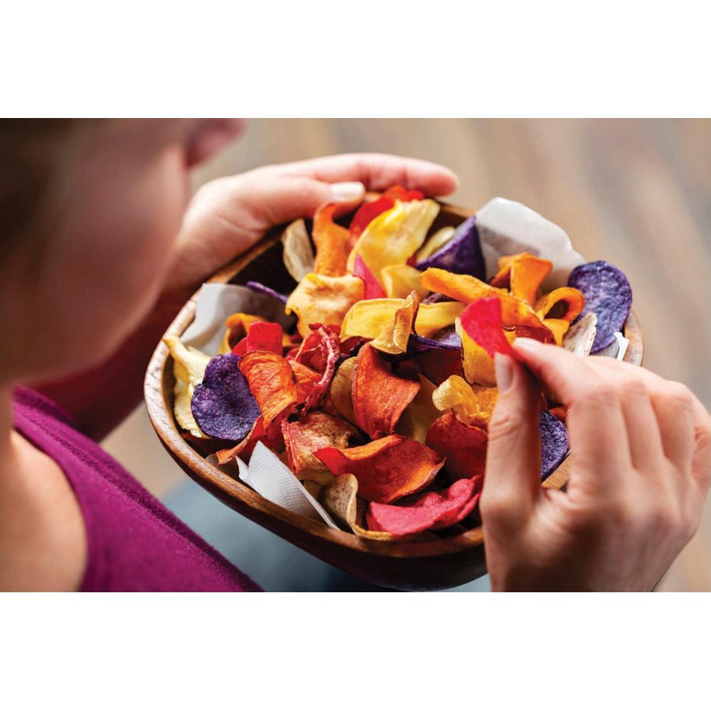 Bunte Gemüschips in einer Schüssel, eine Hand nimmt einen roten Chip.