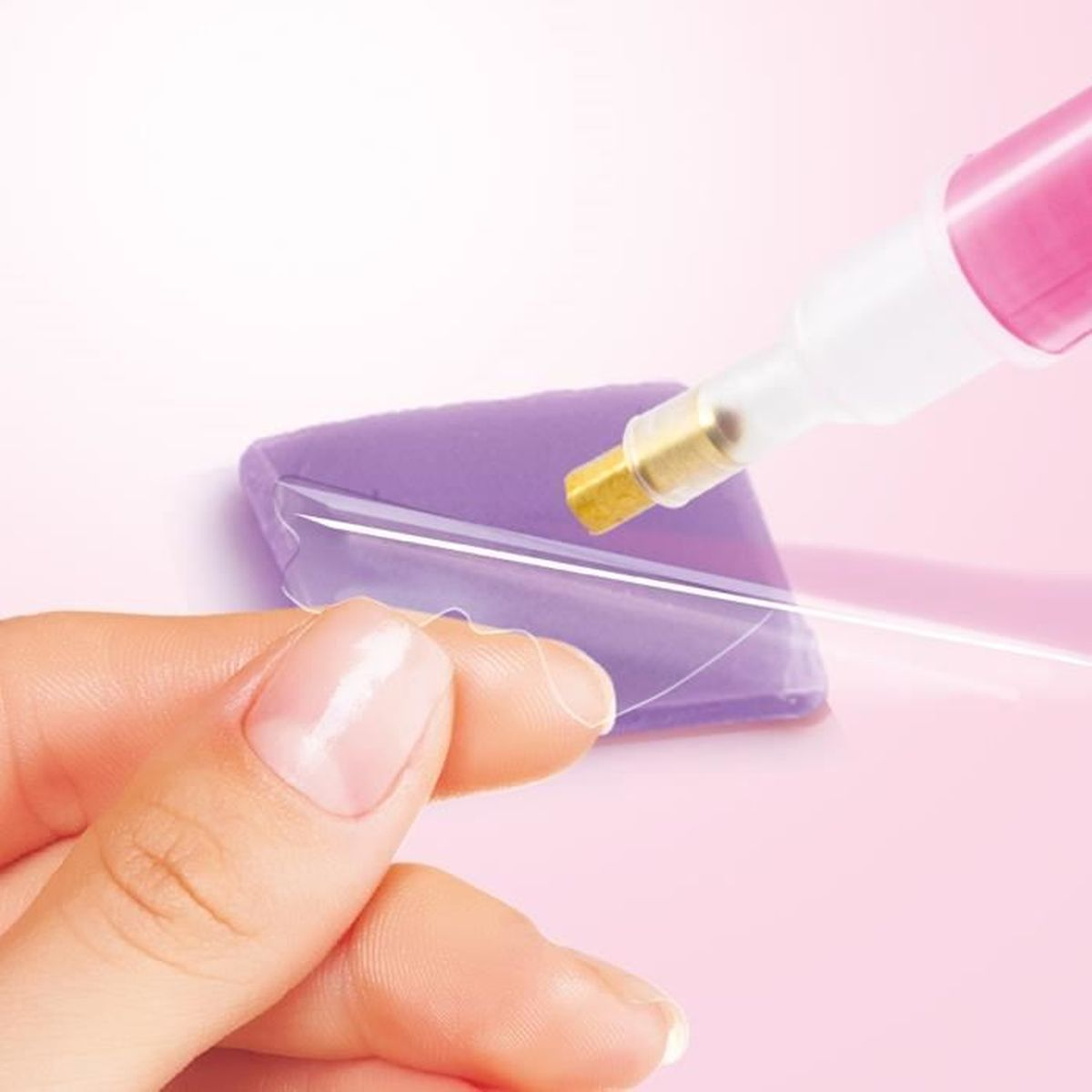 Dłoń trzyma przezroczystą nić nad fioletową poduszką, obok różowego aplikatora.