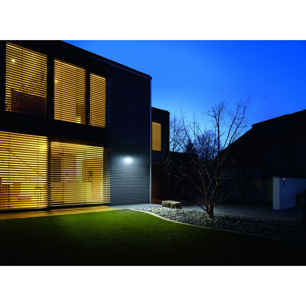 Moderne Hausfassade bei Nacht mit Beleuchtung und Vorgarten.