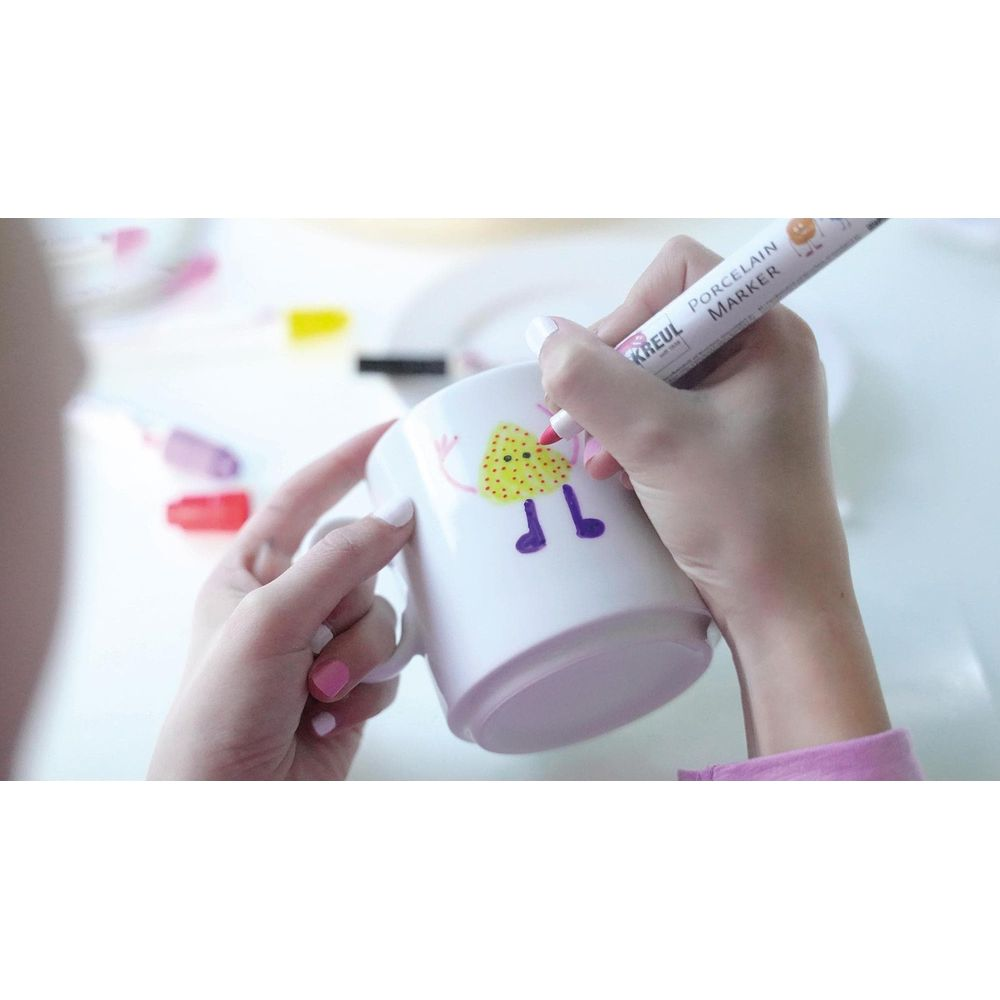 Ręka rysuje żółtą buźkę na białym kubku markerem.