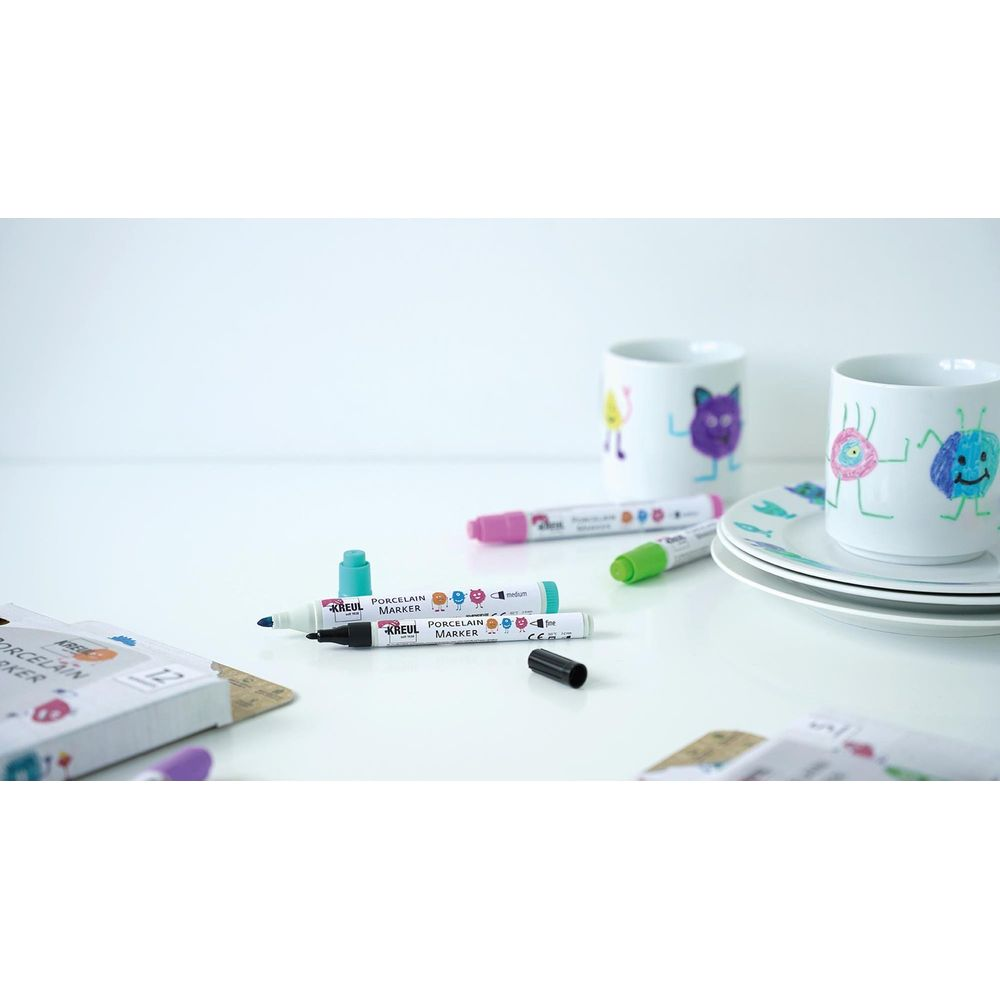 Markery do porcelany w różnych kolorach leżą na stole z ozdobionymi kubkami.
