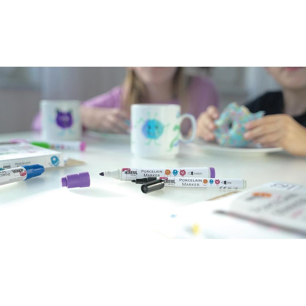 Stół z markerami do porcelany, ozdobionymi kubkami i dzieckiem trzymającym pączka.