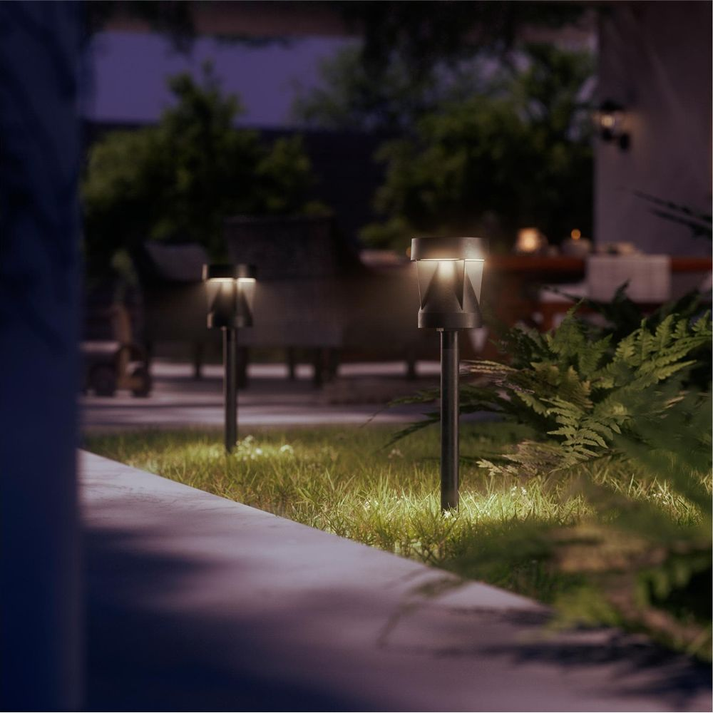 Gartenpfad mit beleuchteten Wegleuchten bei Nacht, mit Pflanzen und Möbeln im Hintergrund.
