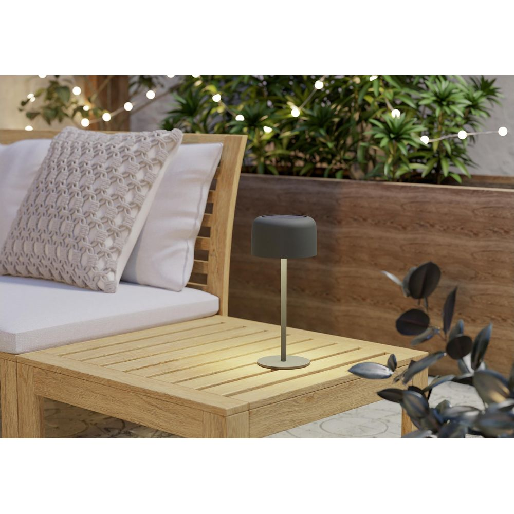 Graue Tischlampe auf Holztisch neben Sofa mit Kissen, Lichterkette im Hintergrund.
