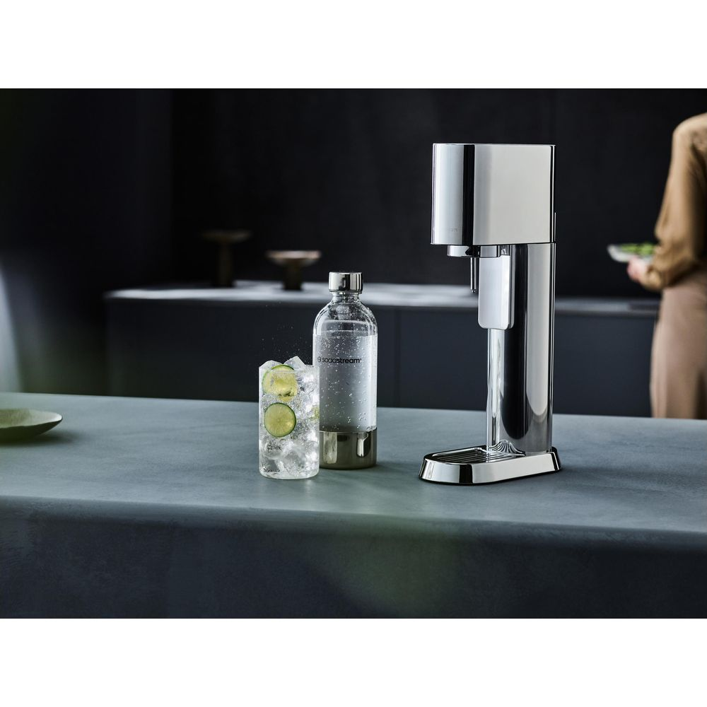 Una macchina per soda accanto a un bicchiere di ghiaccio, lime e acqua frizzante.
