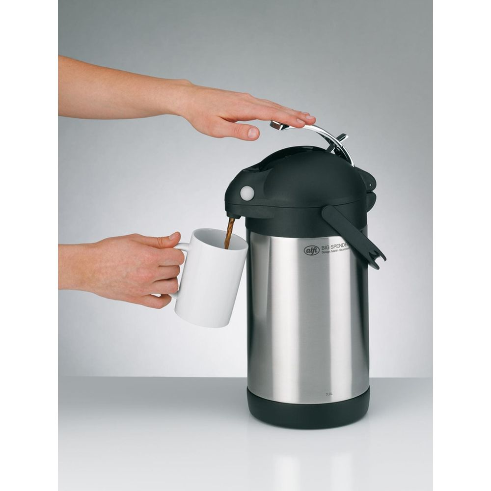 Eine Hand hält eine weiße Tasse, während Kaffee aus einem silbernen Thermosspender gegossen wird.