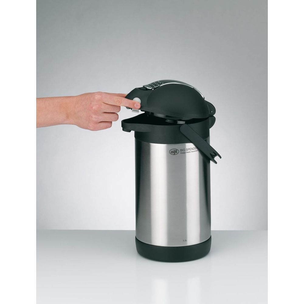 Eine Hand drückt auf den Deckel eines silbernen Thermoskannenspenders.