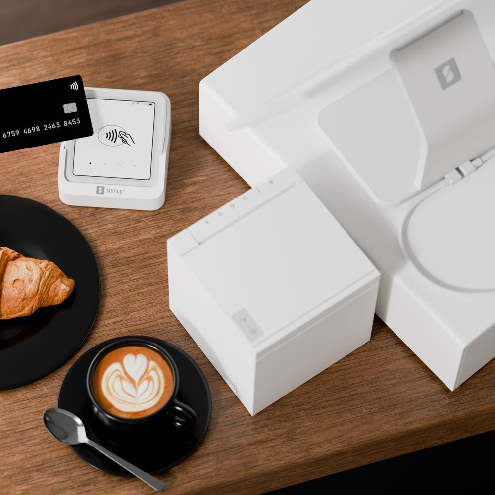Ein Kreditkartenleser, Kaffee, Croissant und ein Kartenleser auf einem Holztisch.