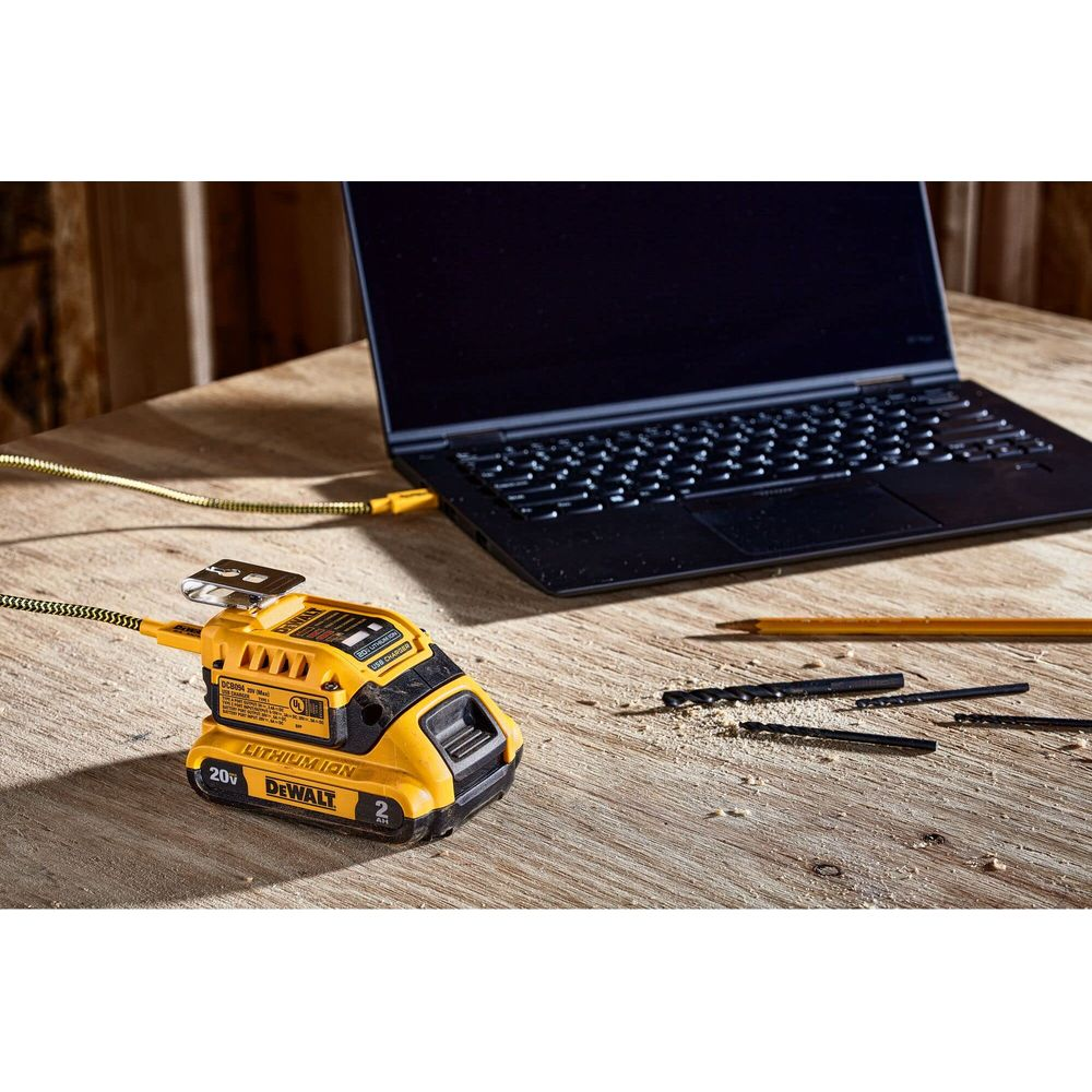 Ein gelber DeWalt-Akku-Adapter ist an einen Laptop angeschlossen. Bohrer liegen daneben.
