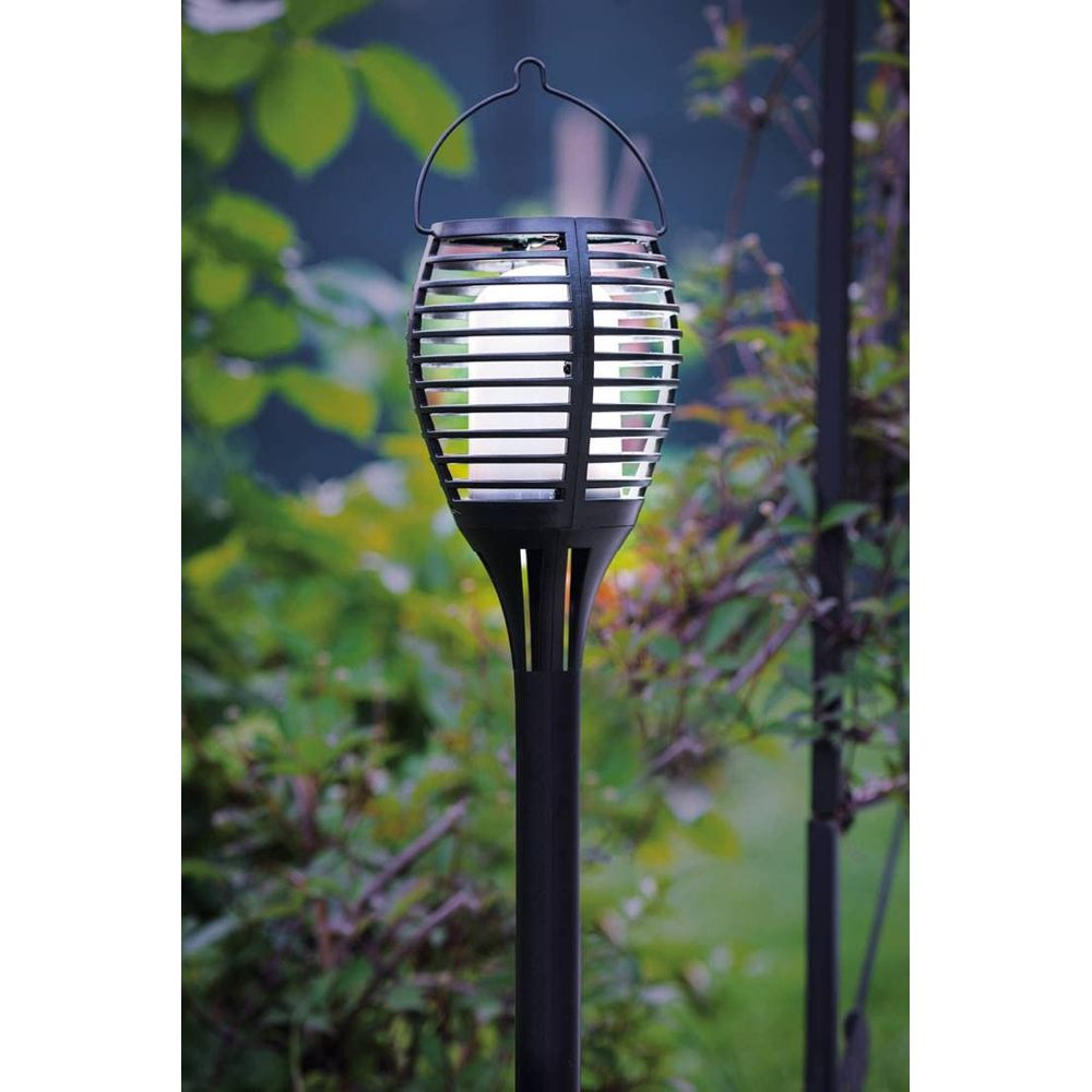 Eine schwarze Gartenfackel mit Laternenschirm steht im Freien.