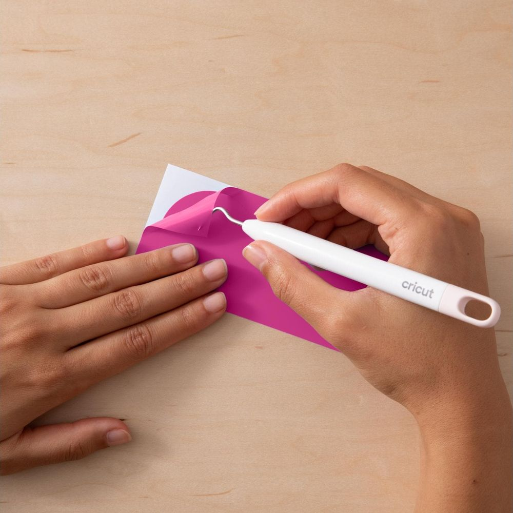 Eine Hand benutzt ein Werkzeug, um pinke Folie von weißem Trägerpapier zu lösen.