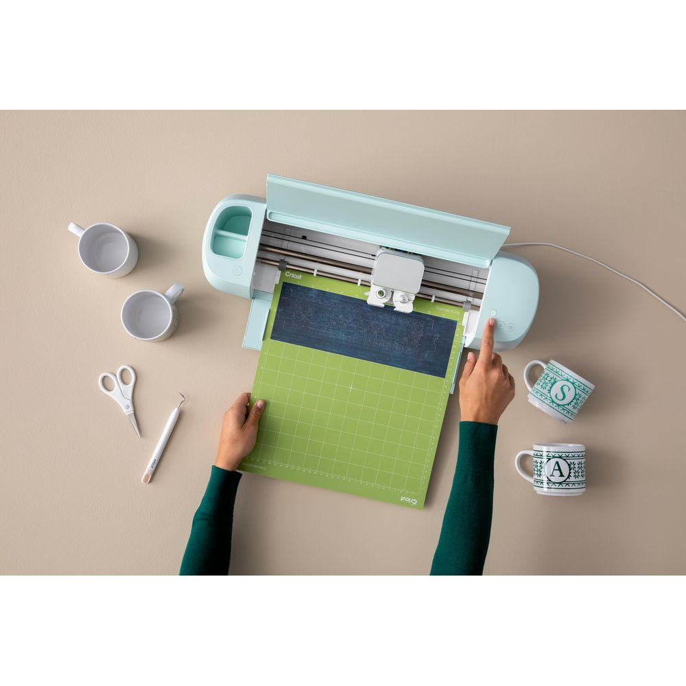 Ein mintgrüner Schneideplotter mit Zubehör und Tassen auf einem Tisch.