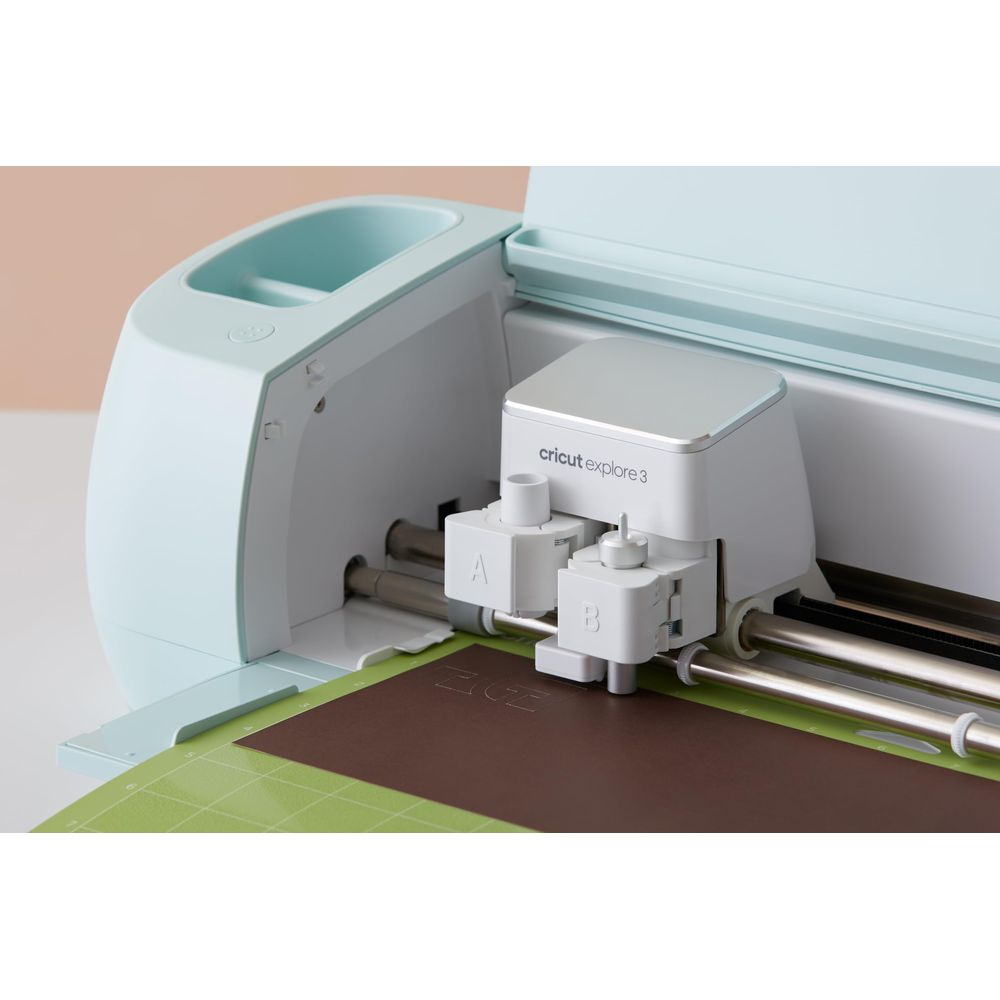 Ein hellblau-weißer Schneideplotter mit der Aufschrift "cricut explore 3" schneidet braunes Papier.