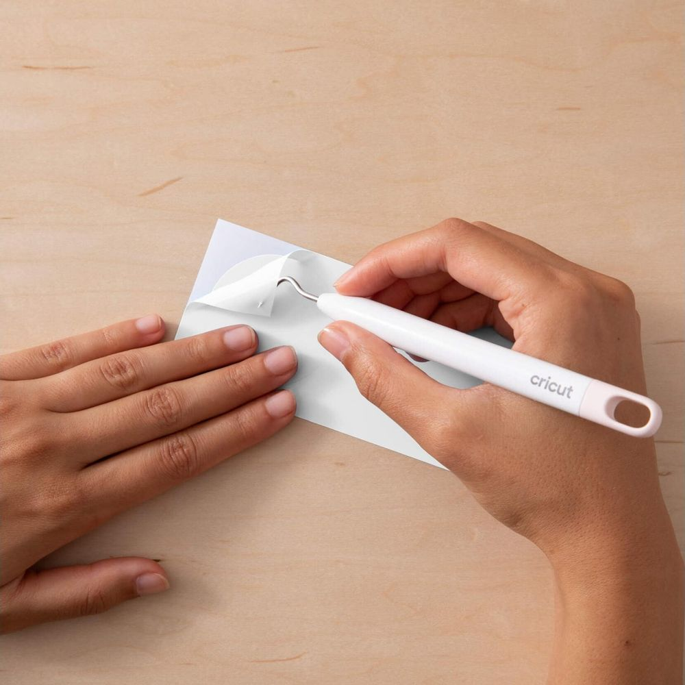 Eine Hand hält ein weißes Werkzeug und schält eine weiße Folie von einem Papier.