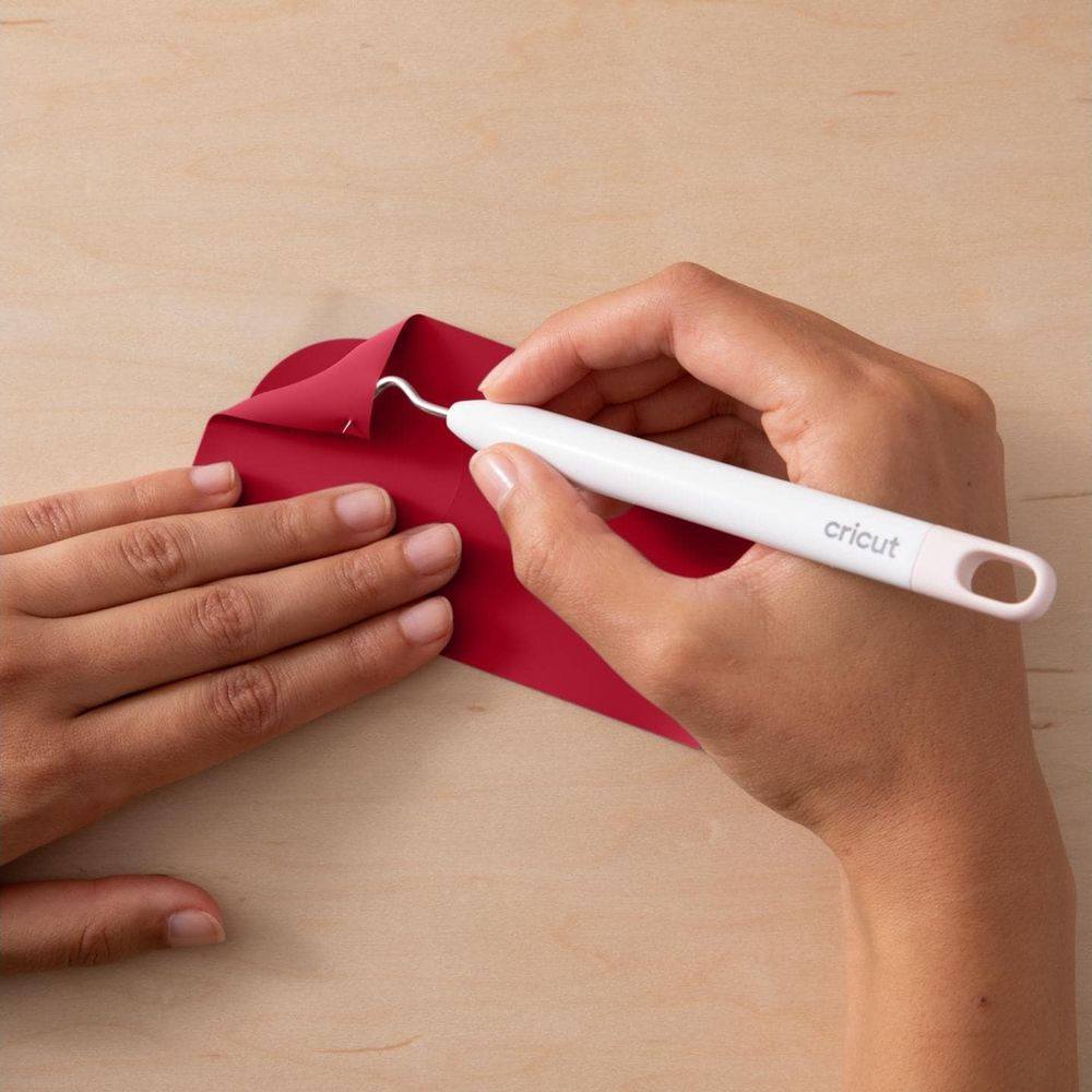 Mains retirant du vinyle rouge avec un outil sur une table en bois.