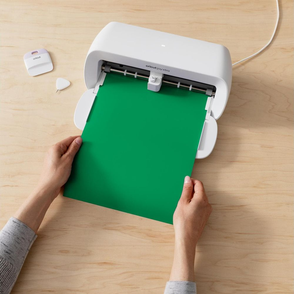 Hände führen grünes Papier in einen weißen Cricut Joy Xtra Cutter ein.