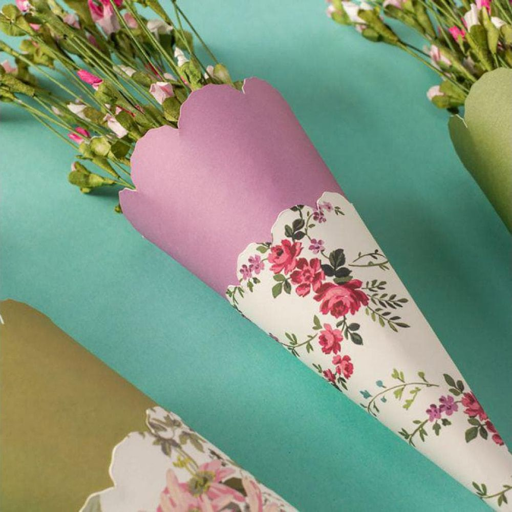 Drei florale Papierkegel halten kleine rosa und weiße Blumen vor einem türkisfarbenen Hintergrund.