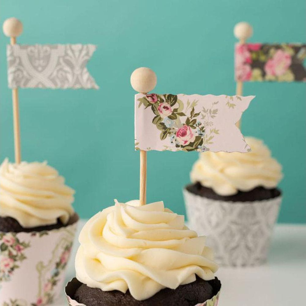 Drei Cupcakes mit cremiger weißer Glasur und dekorativen Fähnchen darauf.