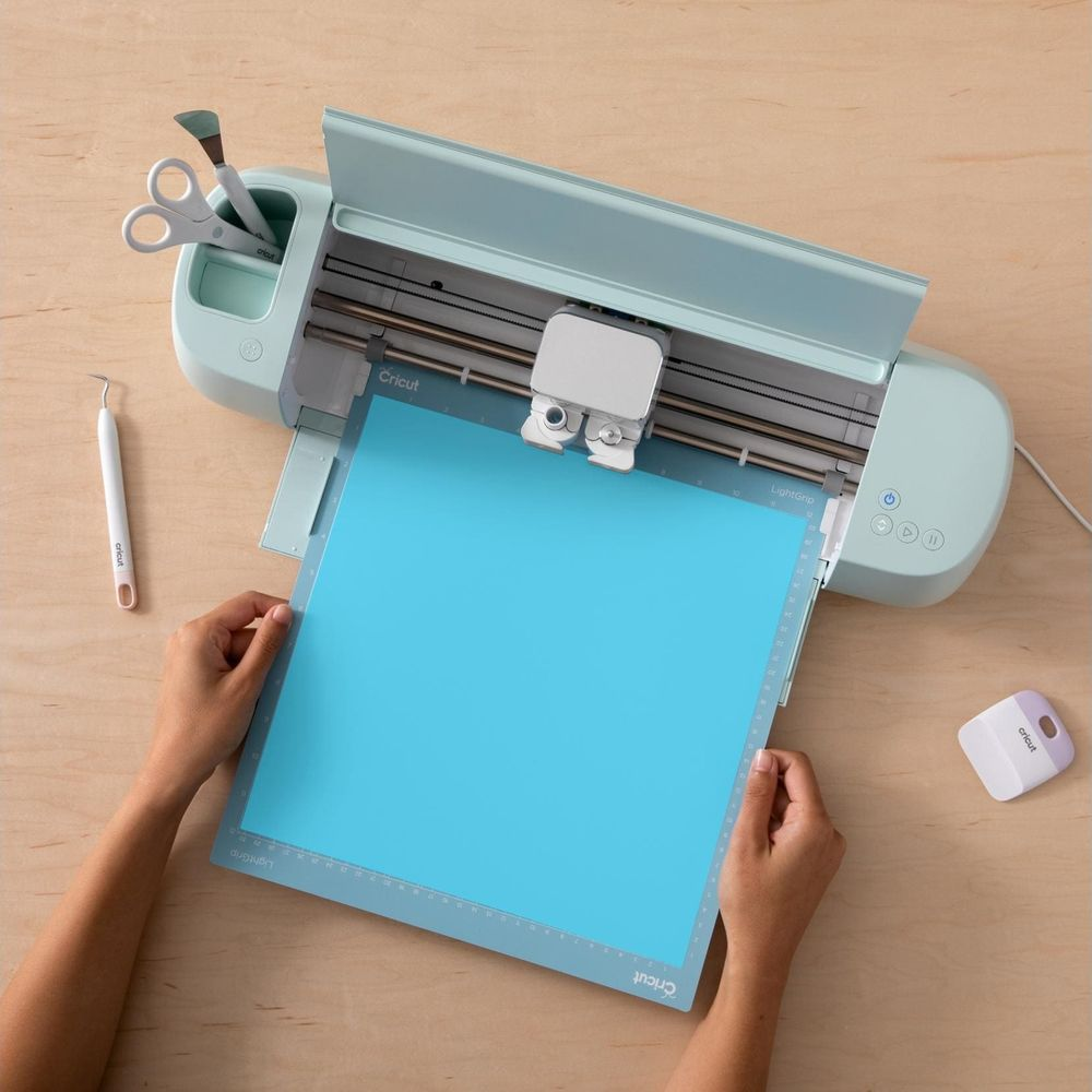 Eine hellblaue Schneidematte wird in eine mintfarbene Schneidemaschine gelegt.