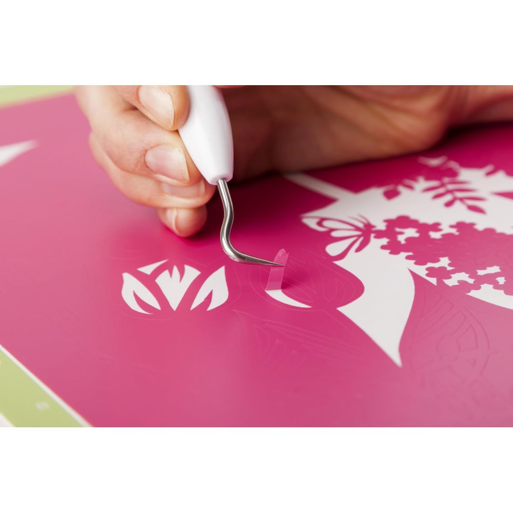 Eine Hand benutzt ein Werkzeug, um Vinyl von einer pinken Matte zu lösen.