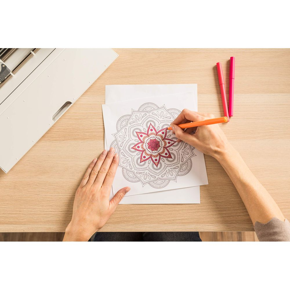 Person malt Mandala mit orangefarbenem Stift. Zwei Stifte liegen daneben.