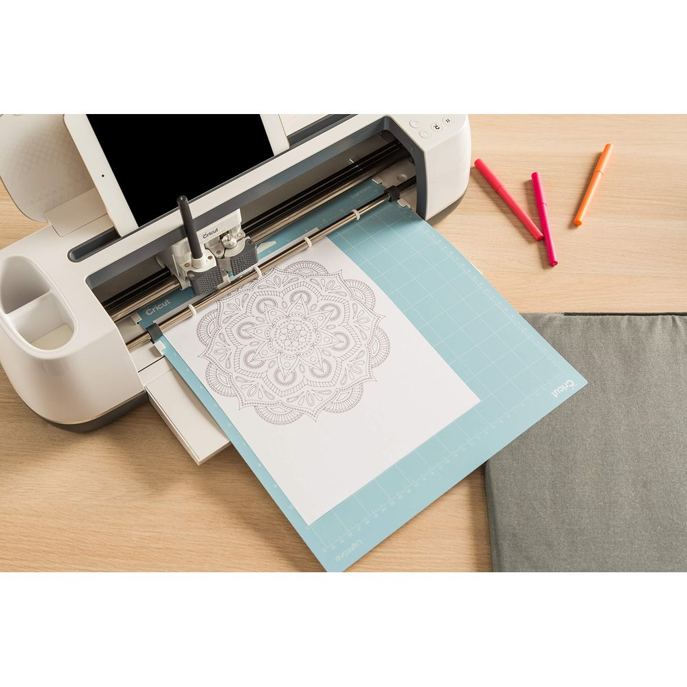 Ein Schneideplotter schneidet ein Mandala auf Papier, daneben liegen Stifte.
