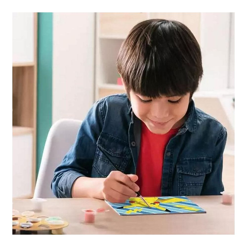Niño pinta a Pikachu en lienzo con pincel y pinturas.