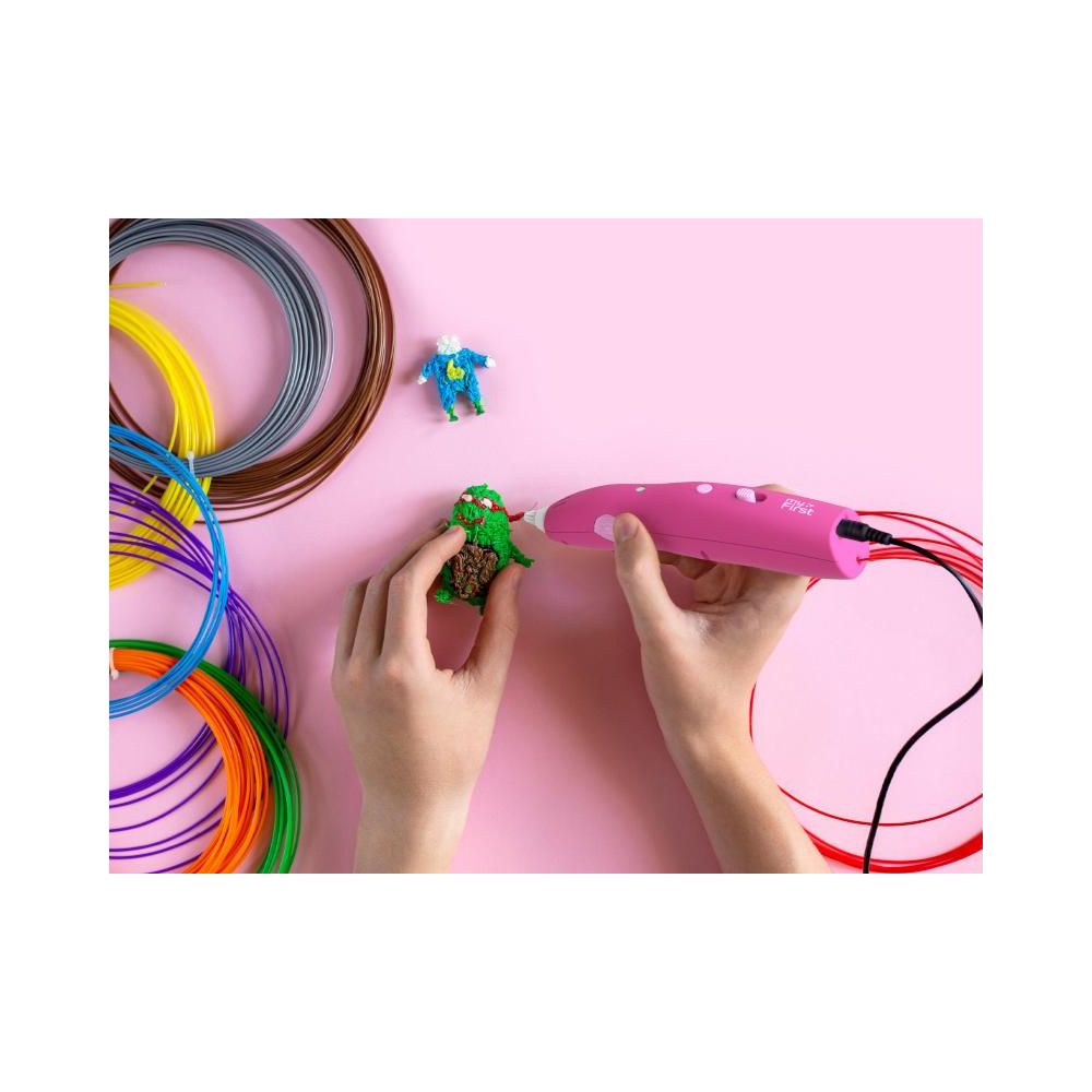 Hände benutzen einen rosa 3D-Stift, um eine grüne Figur zu formen, neben Garnrollen.
