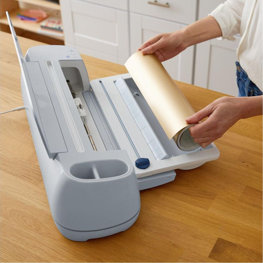 Eine Person legt eine goldene Rolle Papier in ein Schneidegerät ein.
