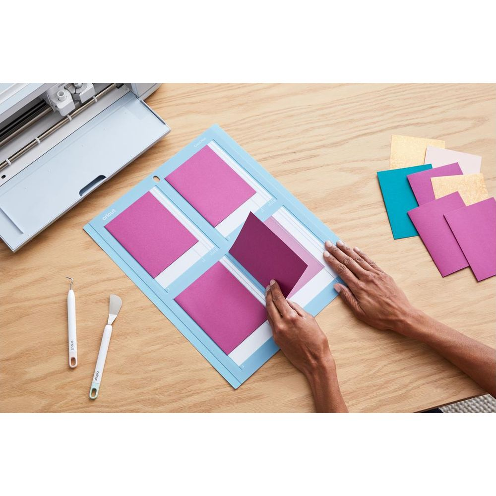 Eine Person legt violette Karten auf eine Schneidematte neben einem Cricut-Gerät.
